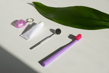 Oral hygiene products and a green leaf on a white table. Toothbrush dental floss dental mirror and dental paste.