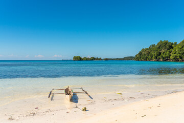 Outrigger canoe on the white sandy beach of the Togian Island Batudaka and view to the islets of Poyalisa in the Gulf of Tomini in Sulawesi. The Islands are a paradise for divers and snorkelers