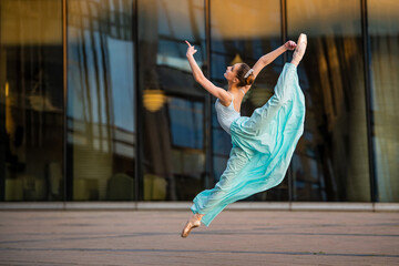 young ballerina in a white leotard is dancing on pointe shoes against the background of a cityscape, frozen in jump