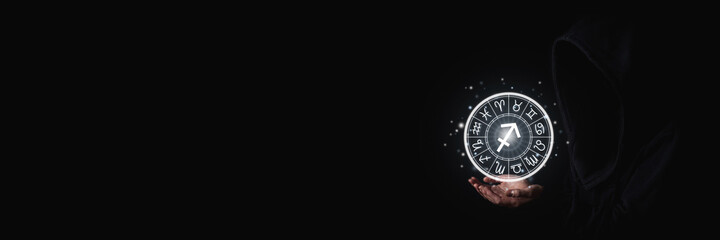Women's hand in the dark holding glowing astrological signs of the zodiac in a circle. Banner