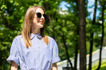 Young woman in dress and glasses stands in the park