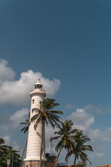 Biała latarnia morska na tle niebieskiego nieba i palm w miejscowości Galle na Sri lance. - obrazy, fototapety, plakaty