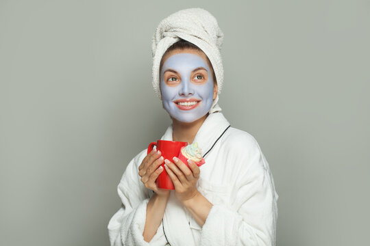 Cheerful optimistic friendly woman in cosmetic face mask eating cupcake and drinking coffee. Female day routine