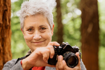 portrait of 70 year old senior woman looking at camera and holding with her hands a photo camera in...