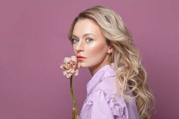 Fashion beauty portrait of pretty woman with healthy skin holding flowers near her face on bright pink background, studio portrait