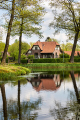 Fototapeta na wymiar Typical dutch authentic old house near the river with reflections in the water, surrounded by trees and greenery creating a mindful scenery on a sunny day during spring in Grientsveen, The Netherlands