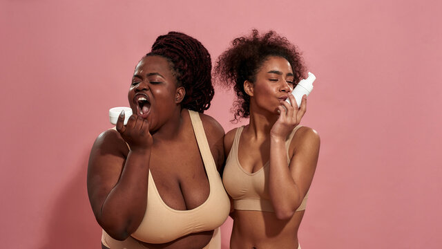 Picture of a plus size afro woman trying to eat a cream and her female friend is kissing a bottle