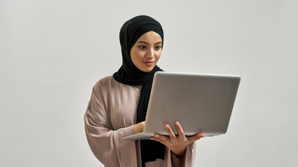 Cute young arabian woman in hijab looking into laptop - obrazy, fototapety, plakaty