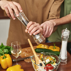 Man peppering salad while cooking with partner
