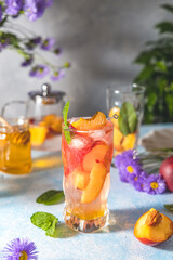 Peach infused water, cocktail, lemonade or tea. Summer iced cold drink with peach and mint on light gray table surface. Selective focus.