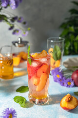 Peach infused water, cocktail, lemonade or tea. Summer iced cold drink with peach and mint on light gray table surface. Selective focus.