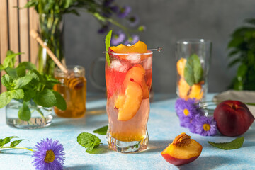 Peach infused water, cocktail, lemonade or tea. Summer iced cold drink with peach and mint on light gray table surface. Selective focus.