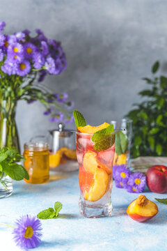 Peach infused water, cocktail, lemonade or tea. Summer iced cold drink with peach and mint on light gray table surface. Selective focus.