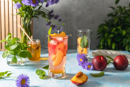 Peach infused water, cocktail, lemonade or tea. Summer iced cold drink with peach and mint on light gray table surface. Selective focus.