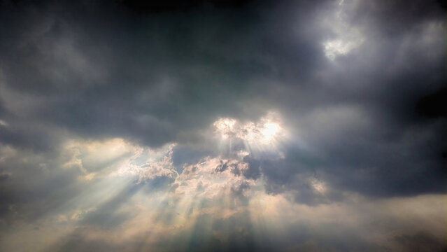 The sky was covered with dark rain clouds and beams of light streaked through the clouds.