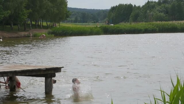 boy jumps into the water of lake near wooden pier. Slow motion video