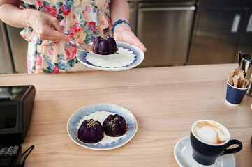 Close-up of female confectioner hands putting a delicious vegan dessert on a plate, standing behind the bar counter. Small business concepts.