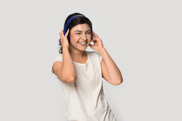 Overjoyed millennial Indian woman isolated on grey studio background wear headphones listen to music online. Smiling young mixed race female in earphones enjoy good quality sound on gadget.