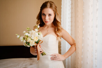 portrait of a beautiful bride with a bouquet by the window. Wedding traditions.