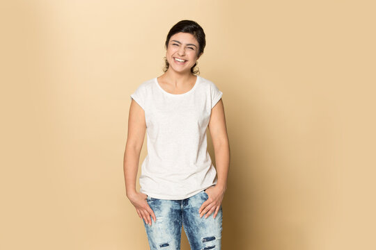 Portrait of overjoyed young Indian woman in casual clothes isolated on yellow studio background laugh at funny joke. Smiling millennial mixed race female feel optimistic. Humor, fun concept.