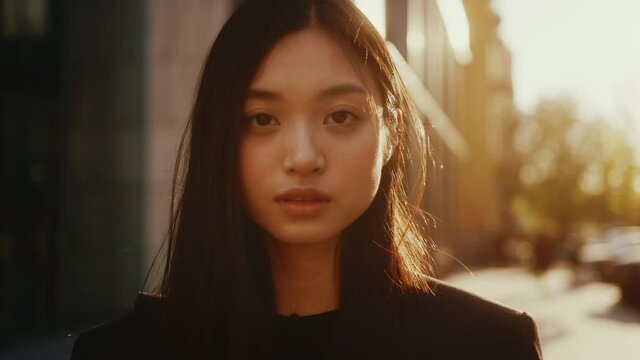Face portrait of beautiful asian young female outdoors. Young pretty mixed-race japanese business woman with black hair posing on the city streets.