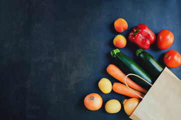 Shopping or delivery healthy food concept. Food supermarket and clean vegan eating concept. Fresh vegetables and fruits: carrot, potato, zucchini, tomato in paper bag on black background. Copy space.