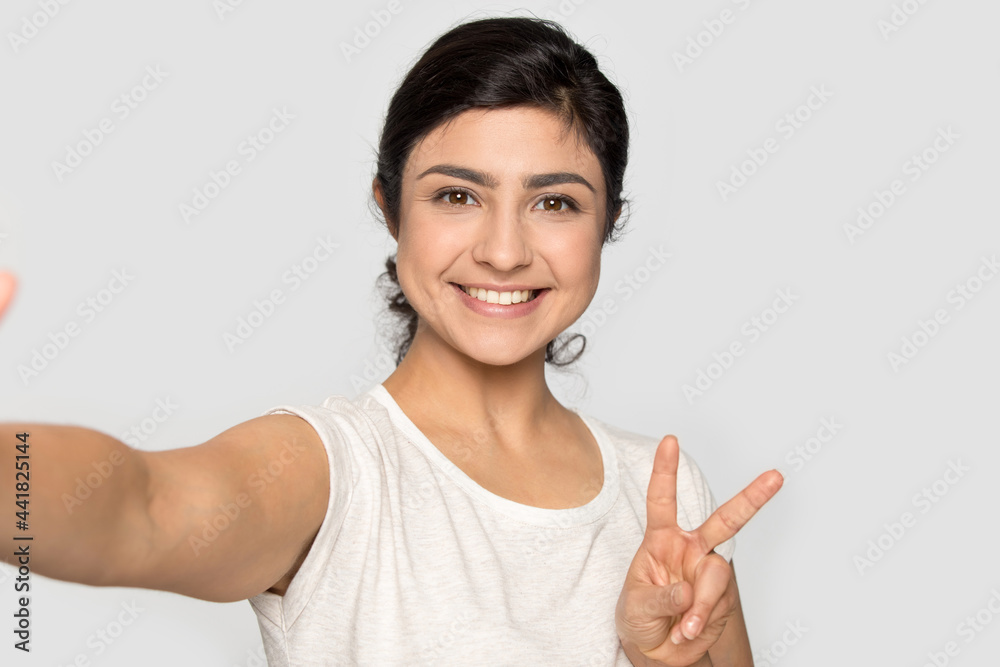 Wall mural smiling indian young woman isolated on grey studio background look at camera make self-portrait pict