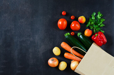Shopping or delivery healthy food concept. Food supermarket and clean vegan eating concept. Fresh vegetables and fruits: carrot, potato, zucchini, tomato in paper bag on black background. Copy space.