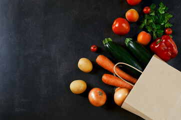 Shopping or delivery healthy food concept. Food supermarket and clean vegan eating concept. Fresh vegetables and fruits: carrot, potato, zucchini, tomato in paper bag on black background. Copy space.