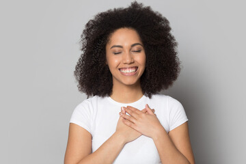 Smiling millennial African American woman isolated on grey studio background keep hands at chest...