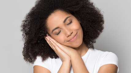 Close up of happy young African American woman isolated on grey studio background fall asleep take nap or daydream. Smiling millennial mixed race female sleep relax feel fatigue. Relaxation concept.