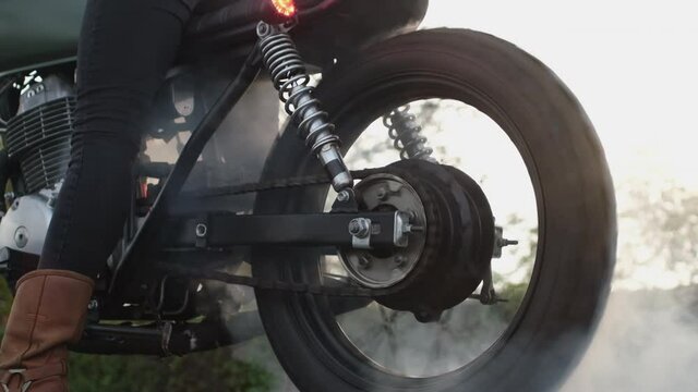 Professional biker stops engine and drifting on asphalt road with clouds of white smoke in evening closeup super slow motion