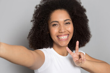 Smiling young African American woman isolated on grey studio background laugh make self-portrait picture on camera. Happy millennial mixed race female take selfie having fun. Diversity concept.