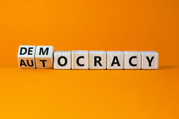 Democracy or autocracy symbol. Turned wooden cubes and changed the word autocracy to democracy. Beautiful orange background, copy space. Business and democracy or autocracy concept.