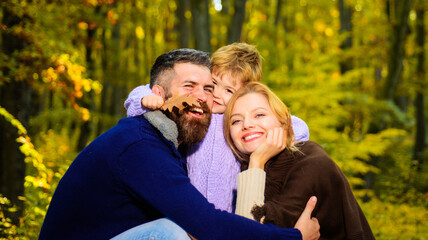 Parents and child together in park on sunny autumn day. Happy family mother and father huggs little son. Happy couple with kid outdoors.