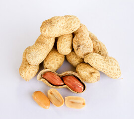 Peanuts stacked separately on a white background . Two kernels have already been removed. One of the peanuts unpacked reveals a red seed on the side.