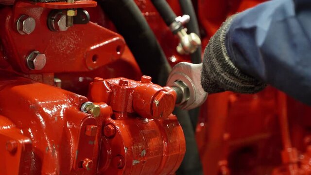 The worker screws the hydraulic hose with a wrench. Production of machinery and agricultural machinery, repair of oil hoses.