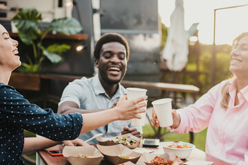 Happy people eating and cheering at food truck restaurant - Focus on left girl face