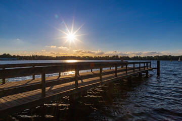 Fototapeta na wymiar Summer landscape with wooden jetty (pier) extend into the Nieuwe meer (New lake) is in southwest of Amsterdam, Beautiful blue sky with golden sunlight before the sunset, Amsterdamse Bos.