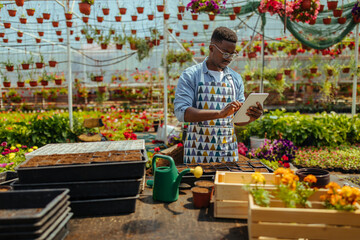 Naklejka premium Gardener with digital tablet in greenhouse