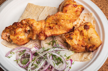 Chicken Meat cooked on skewers. Suvlaki. Shish kebab on a plate with fresh onion rings and pita bread. Grilled chicken meat.
