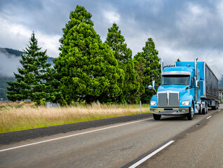 Blue big rig classic semi truck for long haul transporting cargo in covered semi trailer with front...