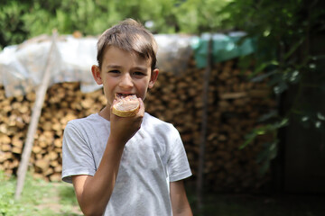 A boy eats a piece of bread smeared with chocolate coating in the nature of a summer sunny day. Close up and copy space