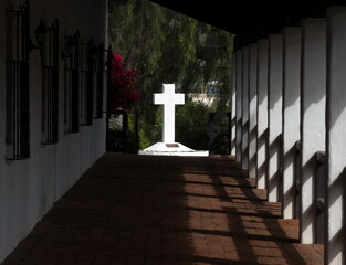 Shades in gallery in front of Mission Basilica San Diego De Alcala lea leading to bright white cross