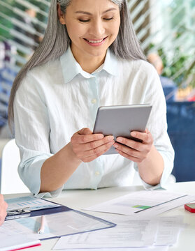 Happy smiling middle aged businesswoman executive manager holding using digital tablet device reading online positive trade news. Business technologies concept. Vertical close up cropped image.