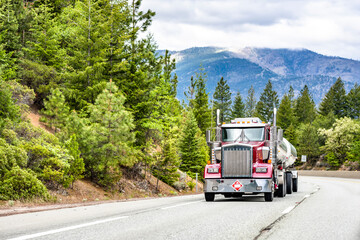 Powerful shiny red big rig classic bonnet semi truck with chrome accessories transporting fuel in...