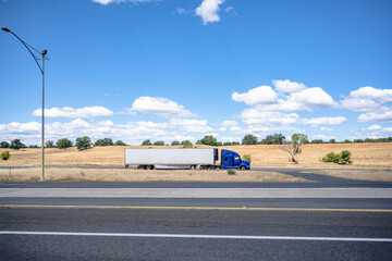 Profile of blue big rig semi truck with refrigerator semi trailer running on the local road with...
