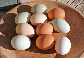 Chicken eggs of different shades lie on  wooden dish.