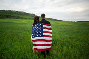 Rear view of young couple wrapped in American flag standing in wheat field