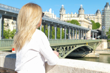 Profile portrait of a blonde woman in the city of Paris. Bir hakeim bridge and historic building...